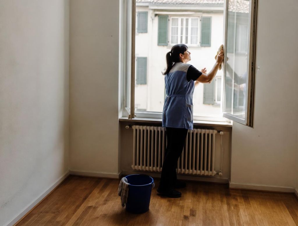 Reinigungskraft putzt ein Fenster in einer leeren Wohnung